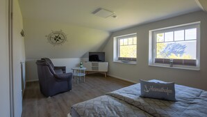 Quarto com cama, escrivaninha, cadeira, janela e um adorno na parede.