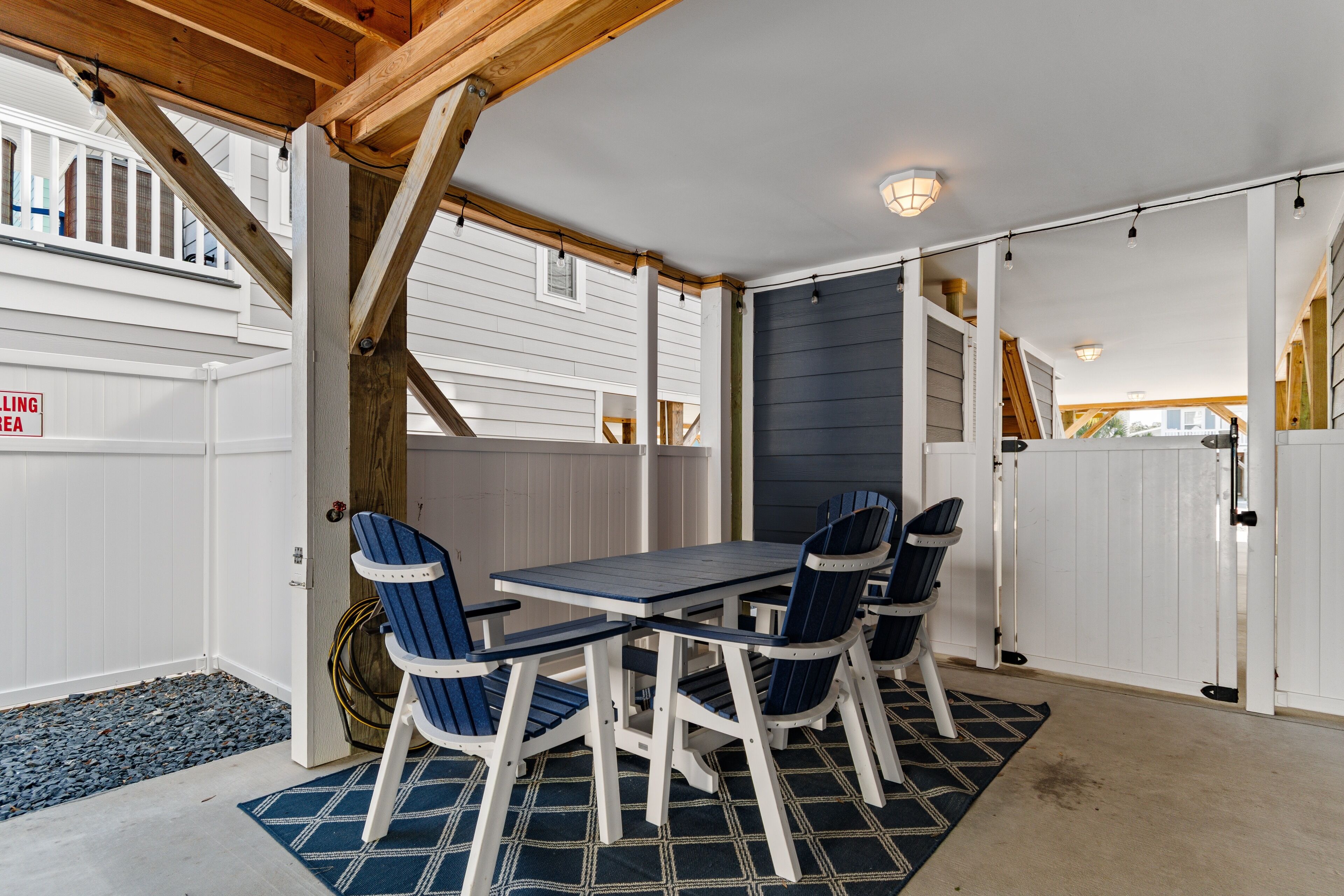 A covered patio area with a table and chairs, wooden beams, and a white fence.