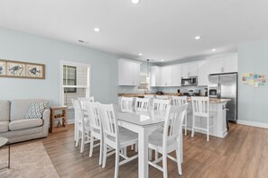 Une cuisine moderne avec des meubles blancs, un réfrigérateur en acier inoxydable et un coin repas comprenant des chaises blanches et une table en verre.
