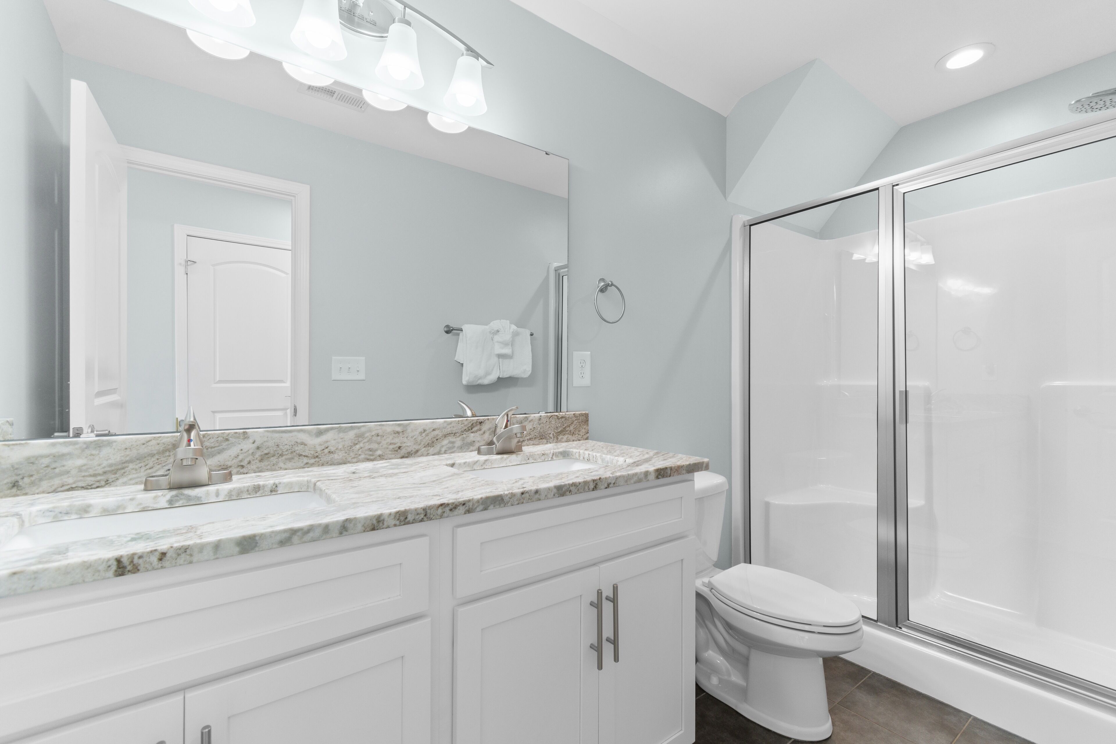 Un baño moderno con un lavamanos de mármol, un espejo grande y una ducha con cerramiento de vidrio.