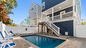 Uma piscina com espreguiçadeiras, um deck de madeira e uma escadaria que leva a uma varanda.