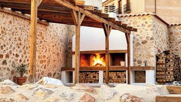 A stone-walled building with a wooden pergola, a fireplace, and a stack of firewood.