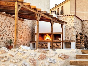 A stone-walled building with a wooden pergola, a fireplace, and a stack of firewood. - Complejo La Serrería (Belmonte)
