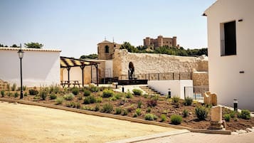 A courtyard with a stone wall, a covered seating area, and a building with a tower.