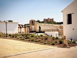 Un patio con muro de piedra, zona de estar techada y un edificio con torre.