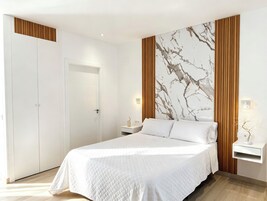 A bedroom with a bed, a nightstand, a wall-mounted light, and a door.