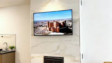 Una sala de estar moderna con un televisor de pantalla plana montado en una pared de mármol, una chimenea y un comedor con una mesa redonda.