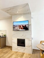 Una sala de estar moderna con un televisor de pantalla plana montado en una pared de mármol, una chimenea y un comedor con una mesa redonda.
