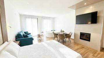 Una habitación de hotel moderna con una cama grande, un sofá, una mesa de comedor con sillas, un televisor de pantalla plana montado en la pared y una chimenea.