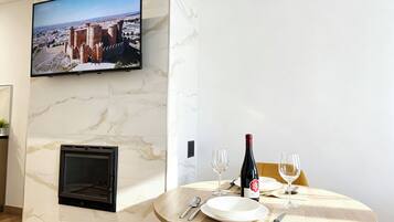 Un comedor con televisor montado en la pared, chimenea y una mesa preparada para dos personas, con copas de vino y una botella.