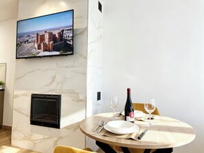 A dining area with a television mounted on the wall, a fireplace, and a table set for two with wine glasses and a bottle. - Complejo La Serrería (Belmonte)