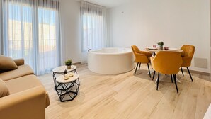 A modern living room with a beige sofa, a round coffee table, a dining table with yellow chairs, and a large white bathtub. - Complejo La Serrería (Belmonte)