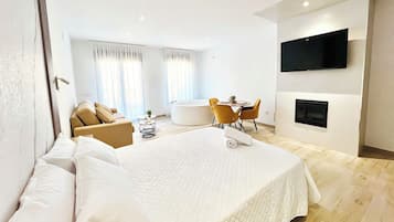 A modern hotel room with a large bed, a seating area with a table, and a flat-screen TV mounted on the wall.