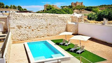 Une piscine avec un mur de pierres en arrière-plan, une pelouse et des chaises longues.
