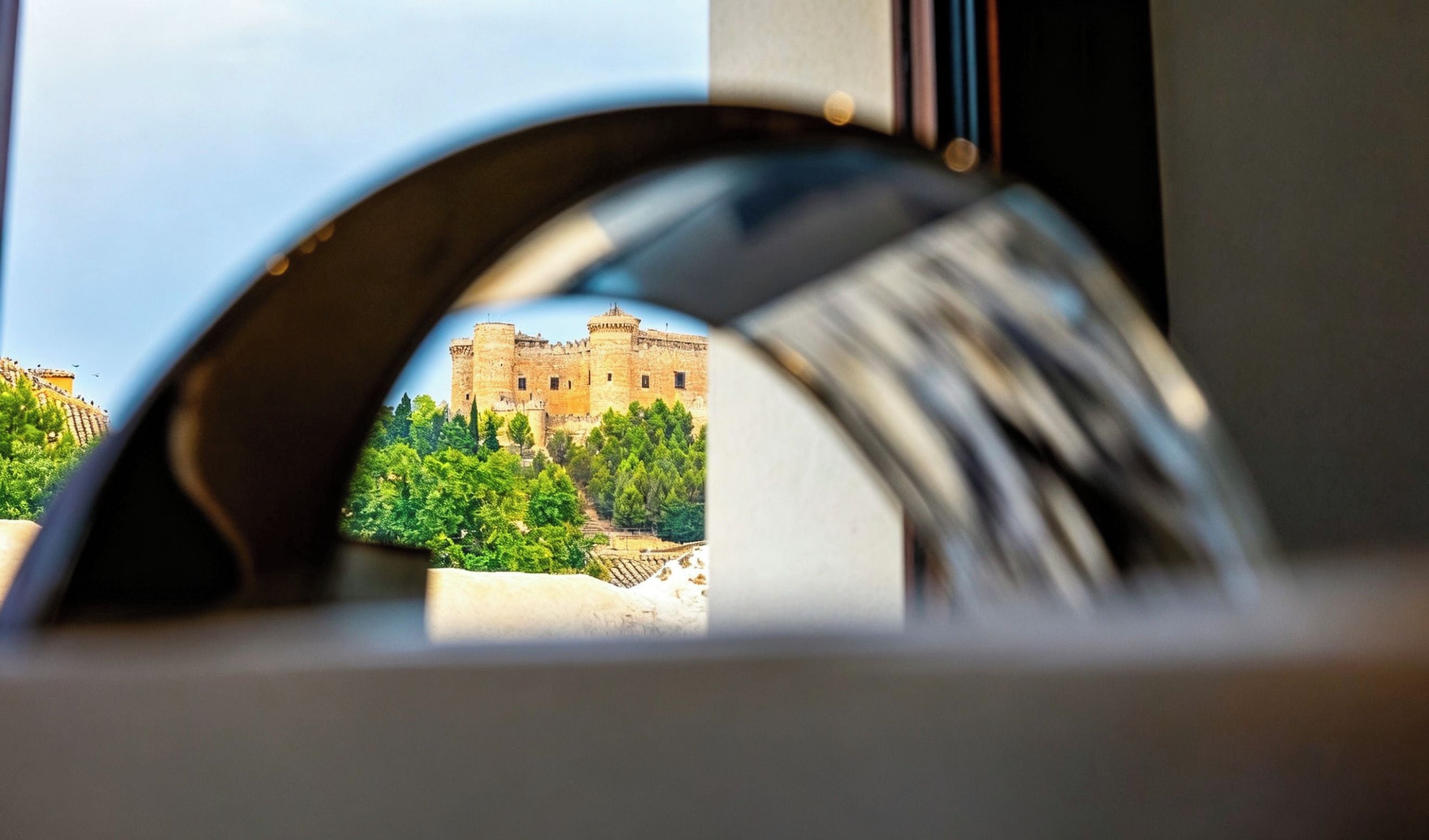A view through a window with a circular frame, focusing on a castle-like building surrounded by greenery.