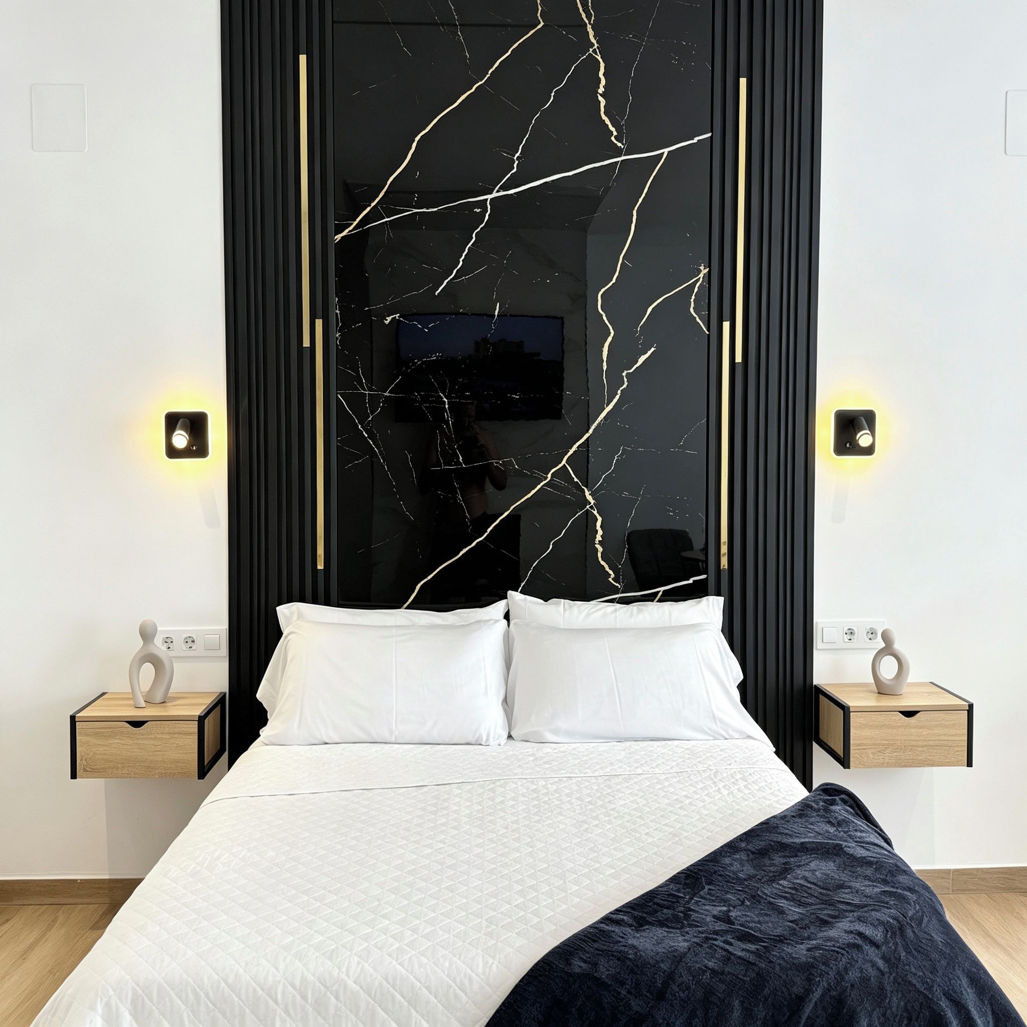 Un dormitorio moderno con una cama grande, dos mesitas de noche y una pared con diseño que imita el mármol negro.
