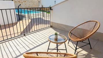 Un balcón con piscina, dos sillas de mimbre y una mesita con una planta.