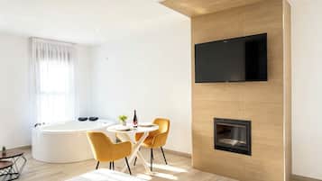 Ein modernes Zimmer mit Kamin, einem an der Wand befestigten Fernseher, einem runden Esstisch mit Stühlen und einer Badewanne.
