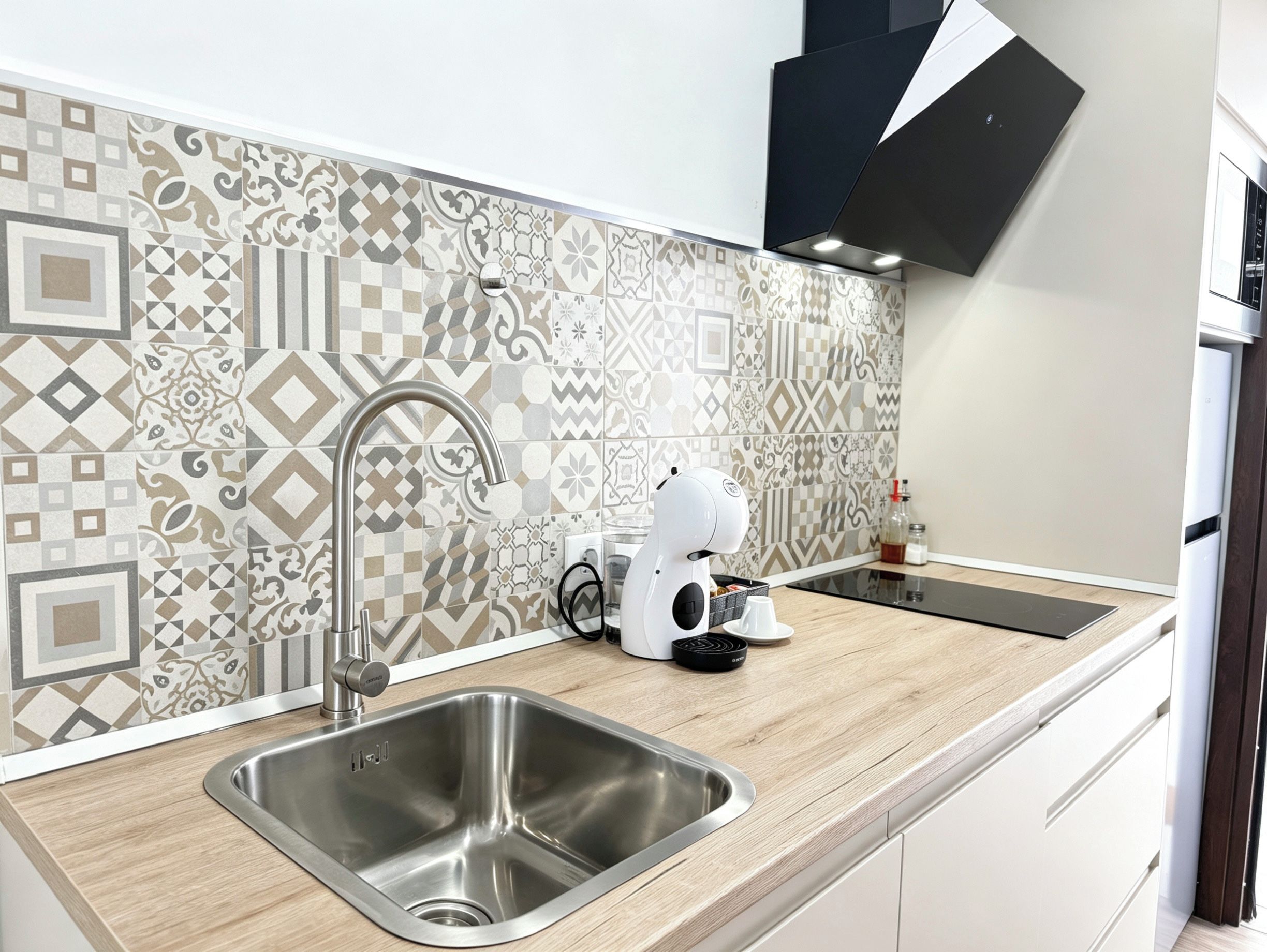 Una cocina moderna con un lavamanos de acero inoxidable, una cafetera y azulejos decorativos en la salpicadero.