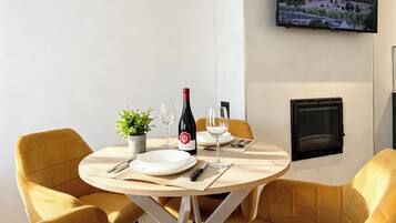 Un comedor con una mesa redonda, sillas amarillas, una botella de vino, copas de vino, una pequeña planta en maceta y un televisor de pantalla plana montado en la pared.