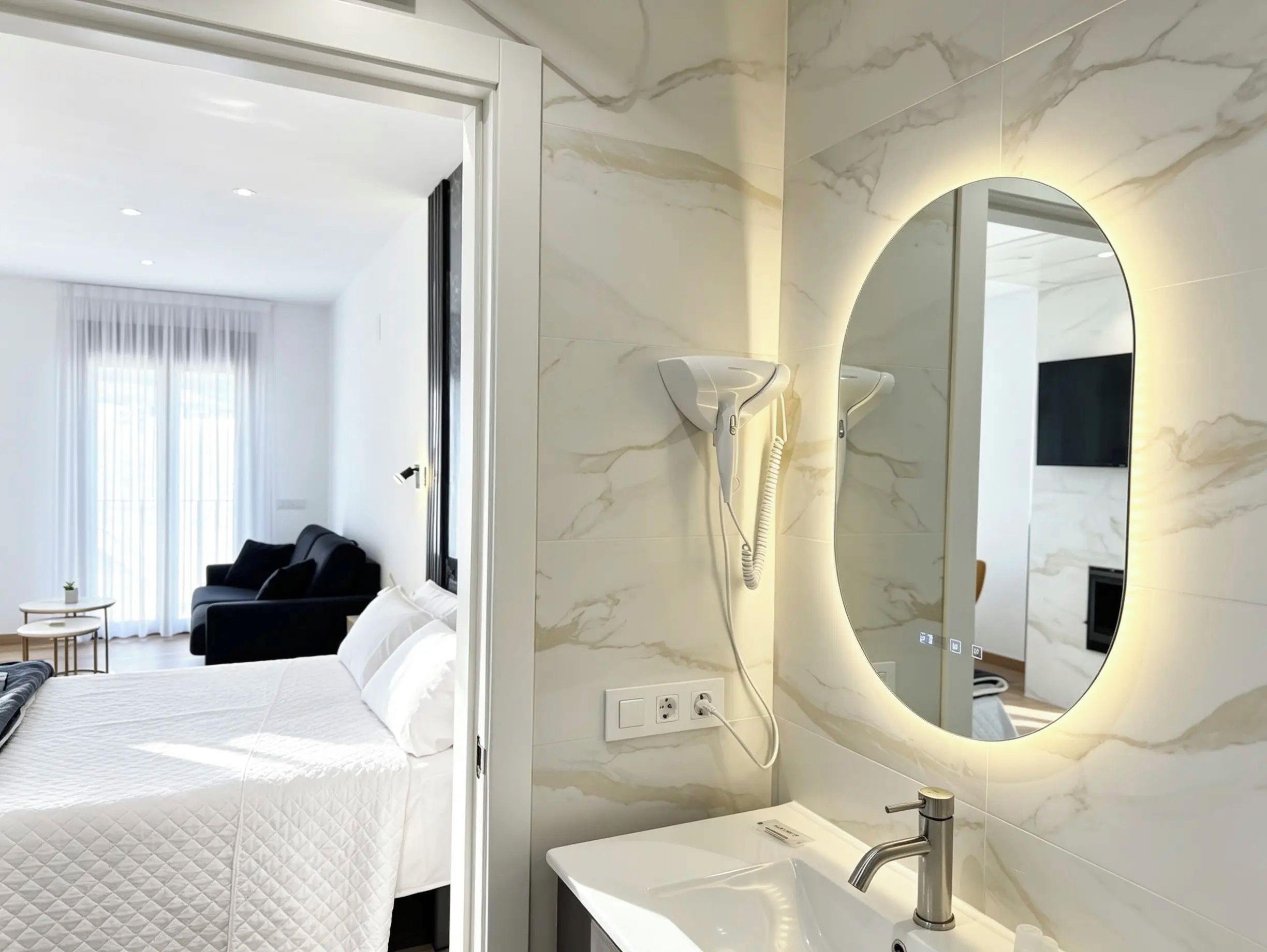 A hotel room with a bed, a bedside table, a mirror, a hairdryer, and a TV mounted on the wall.
