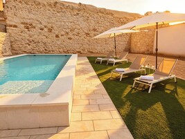 Una piscina con sillones de descanso y un muro de piedra.