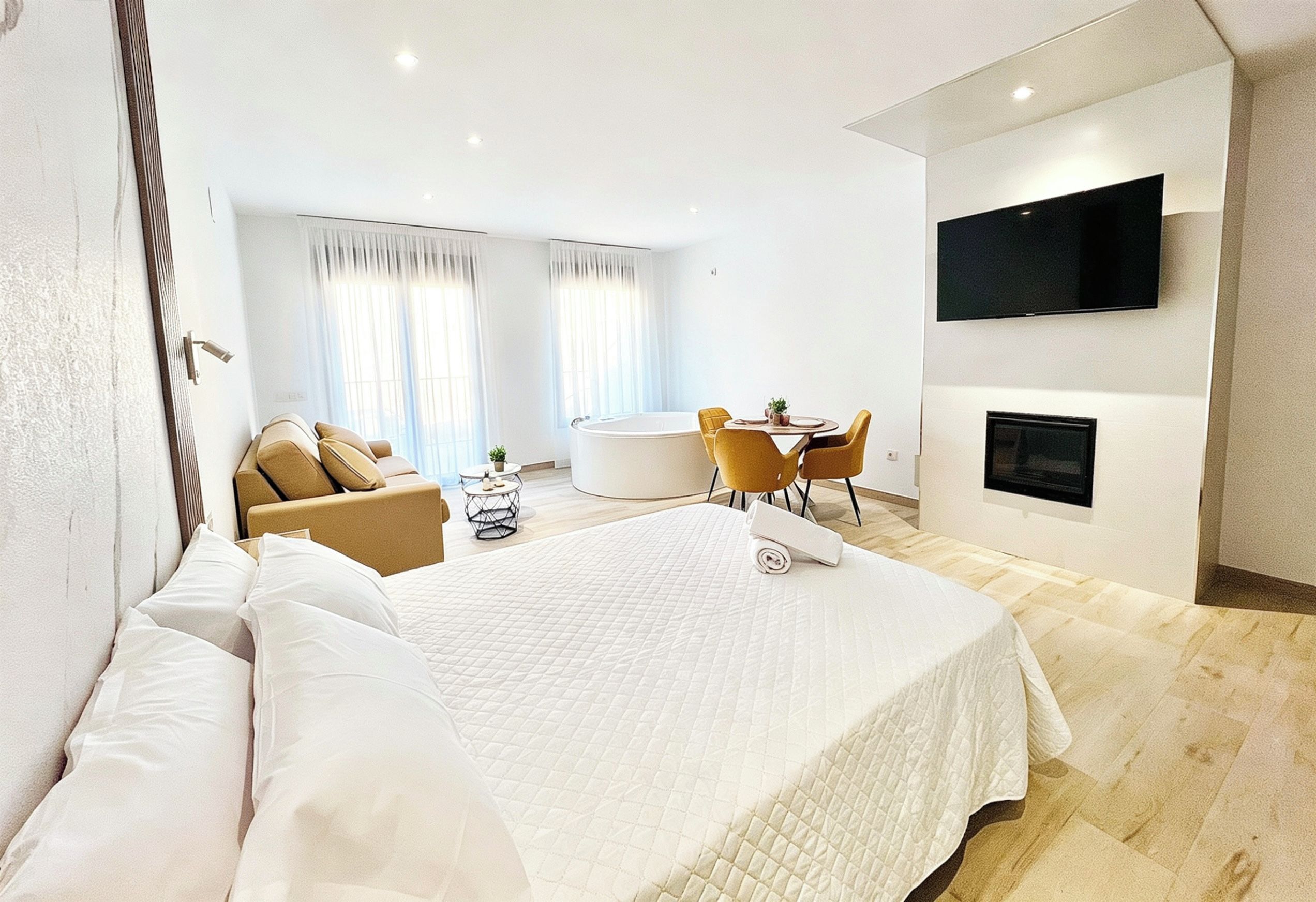 Una habitación de hotel moderna con una cama grande, una zona de estar con una mesa y un televisor de pantalla plana en la pared.