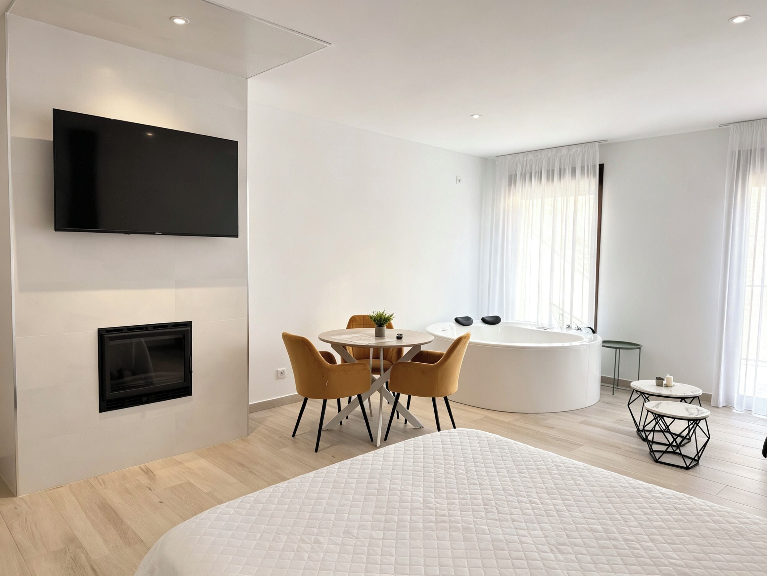 Una habitación de hotel moderna con una televisión de pantalla plana, una mesa de comedor redonda, un sofá, una bañera y una pequeña mesa redonda con una vela.
