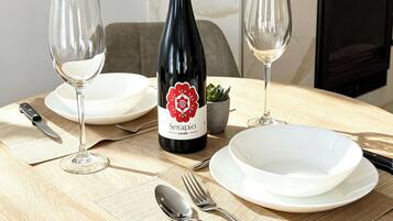 Una mesa de comedor con una botella de vino, dos copas de vino, platos, cubiertos y una pequeña planta en maceta.