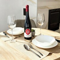 Una mesa de comedor con una botella de vino, dos copas de vino, platos, cubiertos y una pequeña planta en maceta.