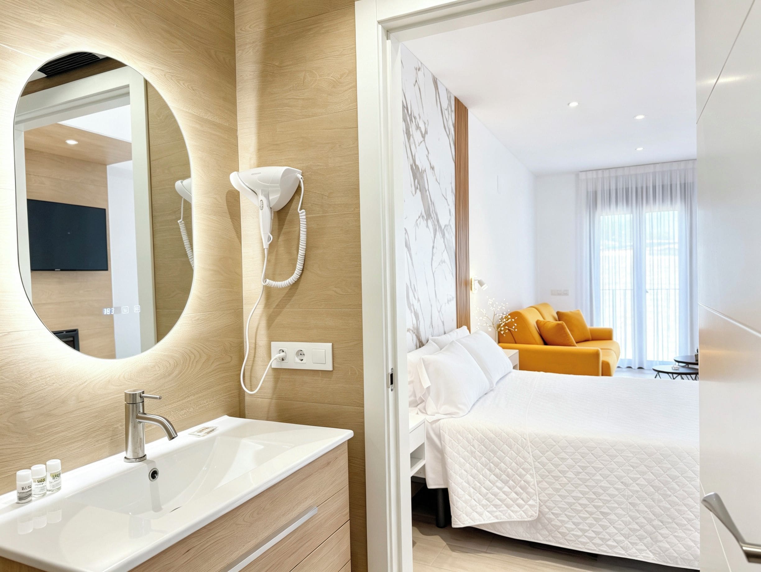 Una habitación de hotel moderna con una cama grande, un baño con lavamanos y espejo, y un teléfono.