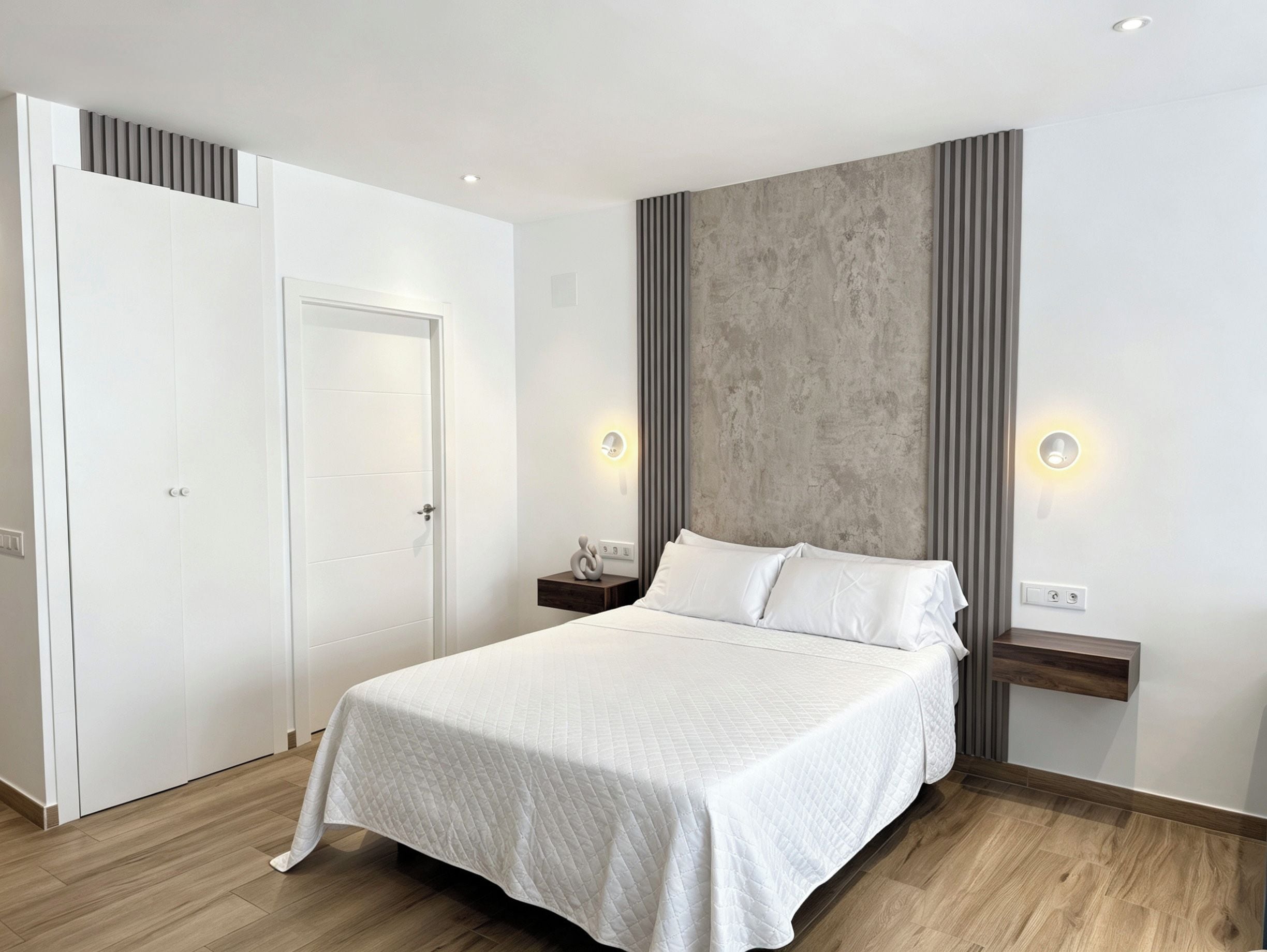 Une chambre moderne avec un grand lit, une armoire et un mur d’accent en béton.