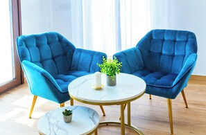 Una habitación con dos sillones azules, una mesita redonda y una planta en maceta.