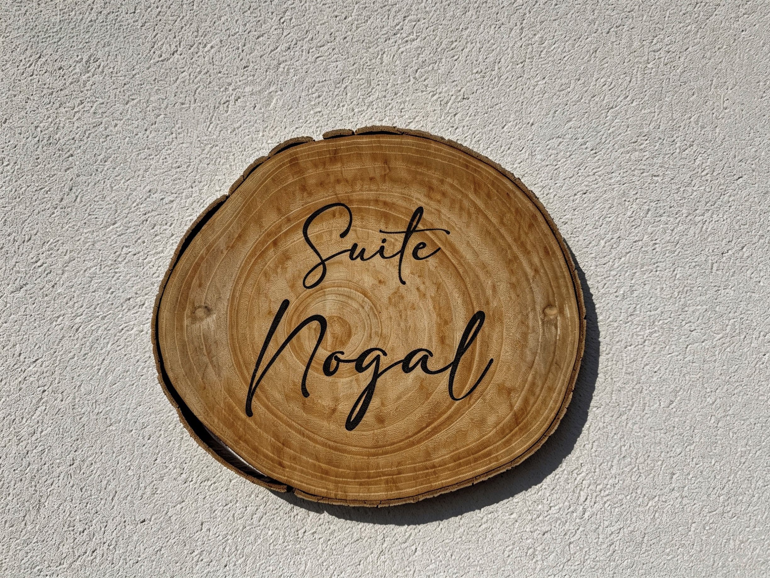 Un letrero de madera con el texto 'Suite Nogal' sobre una pared con textura.