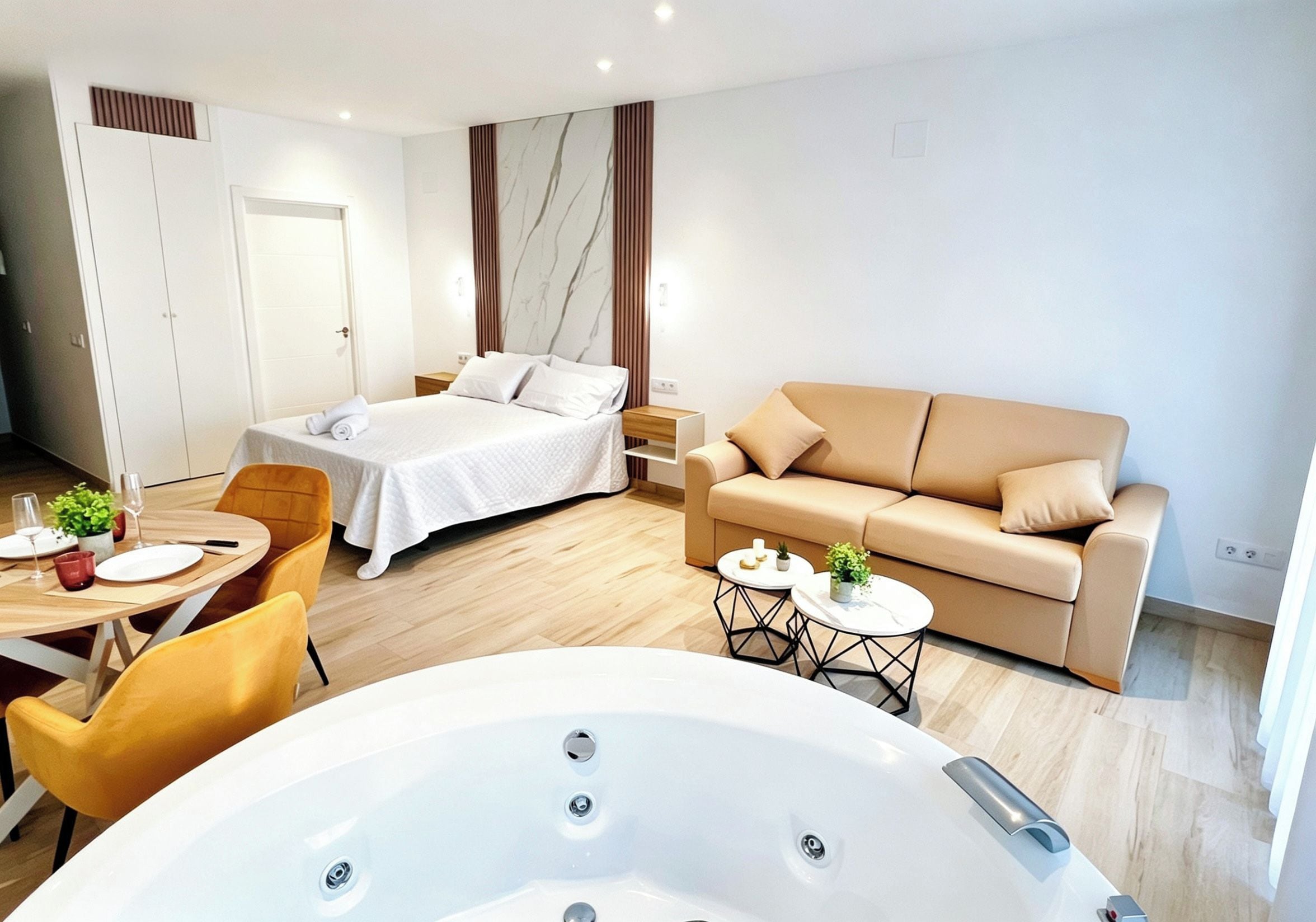 Una habitación de hotel moderna con cama, sofá, zona de comedor y bañera de hidromasaje.