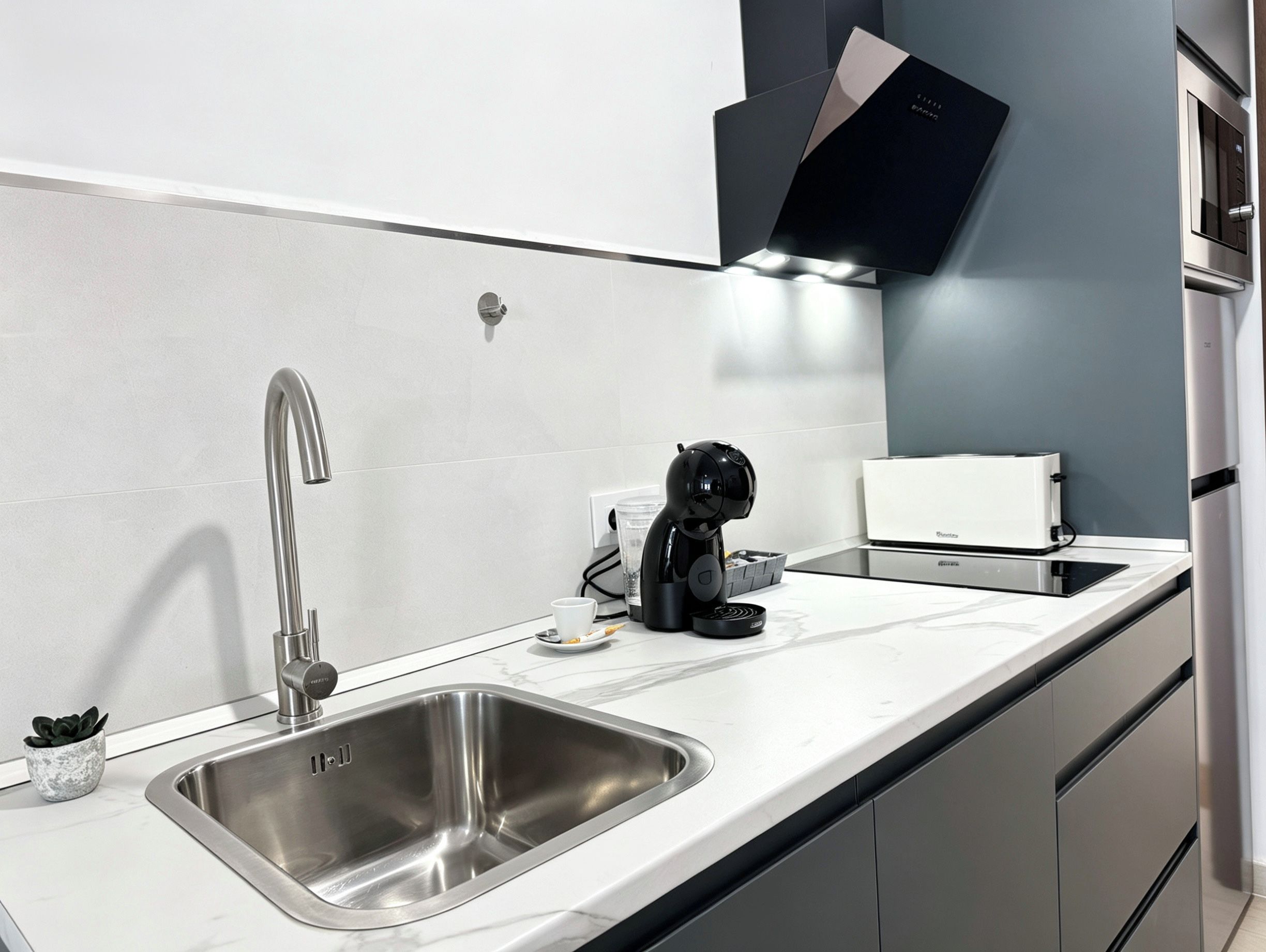 Una cocina moderna con un lavamanos de acero inoxidable, una cafetera y un tostador.