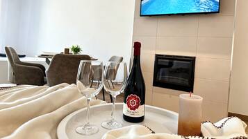 Habitación de hotel con una televisión mostrando una piscina, una botella de vino, dos copas y una vela sobre una bandeja.