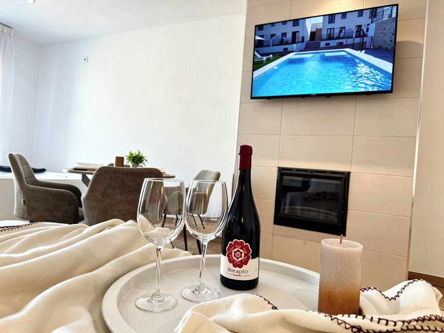 A hotel room with a television displaying a pool, a bottle of wine, two glasses, and a candle on a tray.