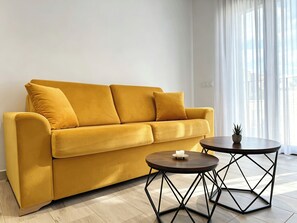 A yellow sofa with three cushions, a small round table with a candle, and a potted plant. - Complejo La Serrería (Belmonte)