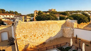 A stone wall with a metal railing, a small garden area with a lamp post, and a view of a town with buildings and a tower in the distance. - Complejo La Serrería (Belmonte)