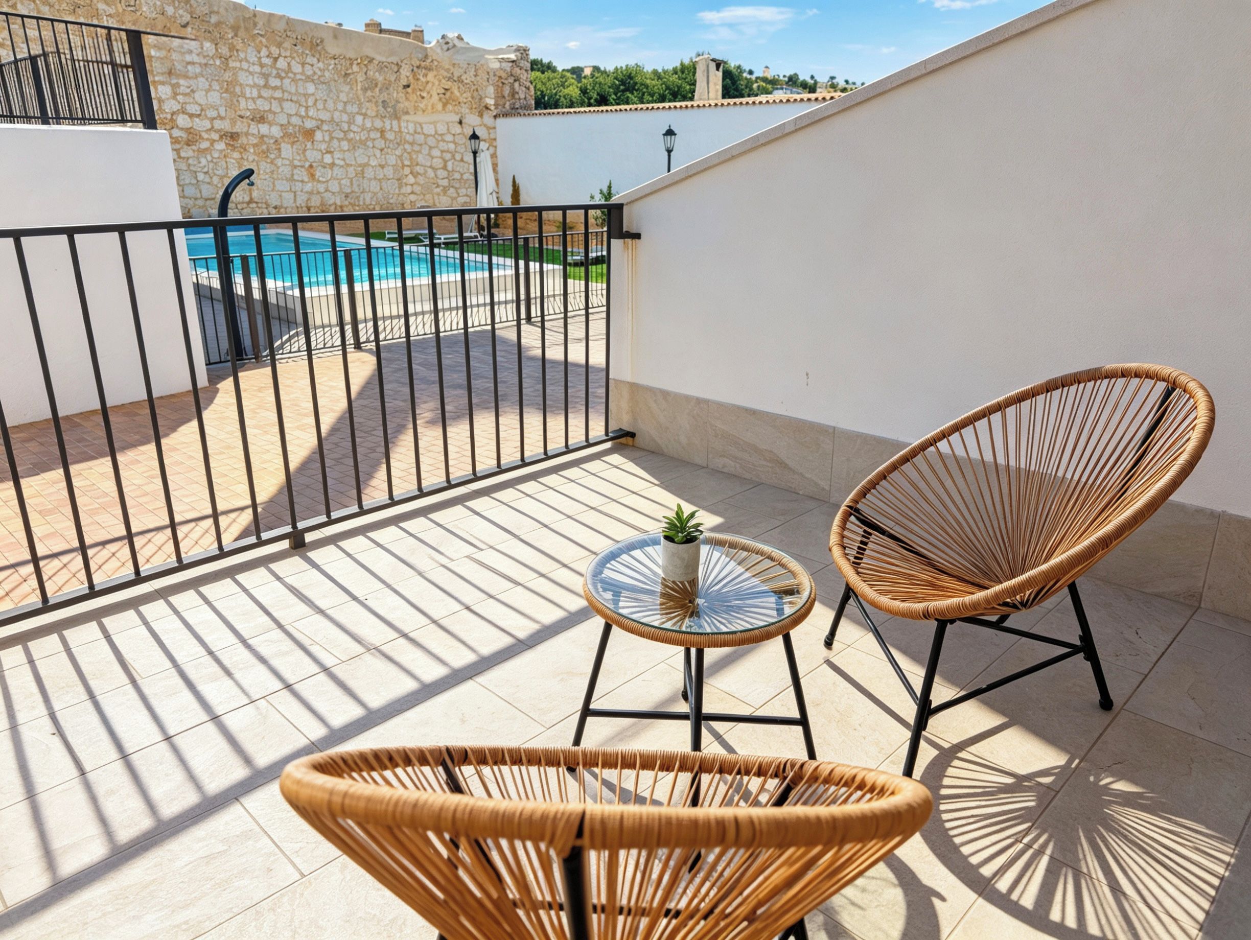 Un balcon avec une piscine, deux fauteuils en osier et une petite table agrémentée d’une plante.