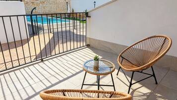 Un balcon avec une piscine, deux fauteuils en osier et une petite table agrémentée d’une plante.