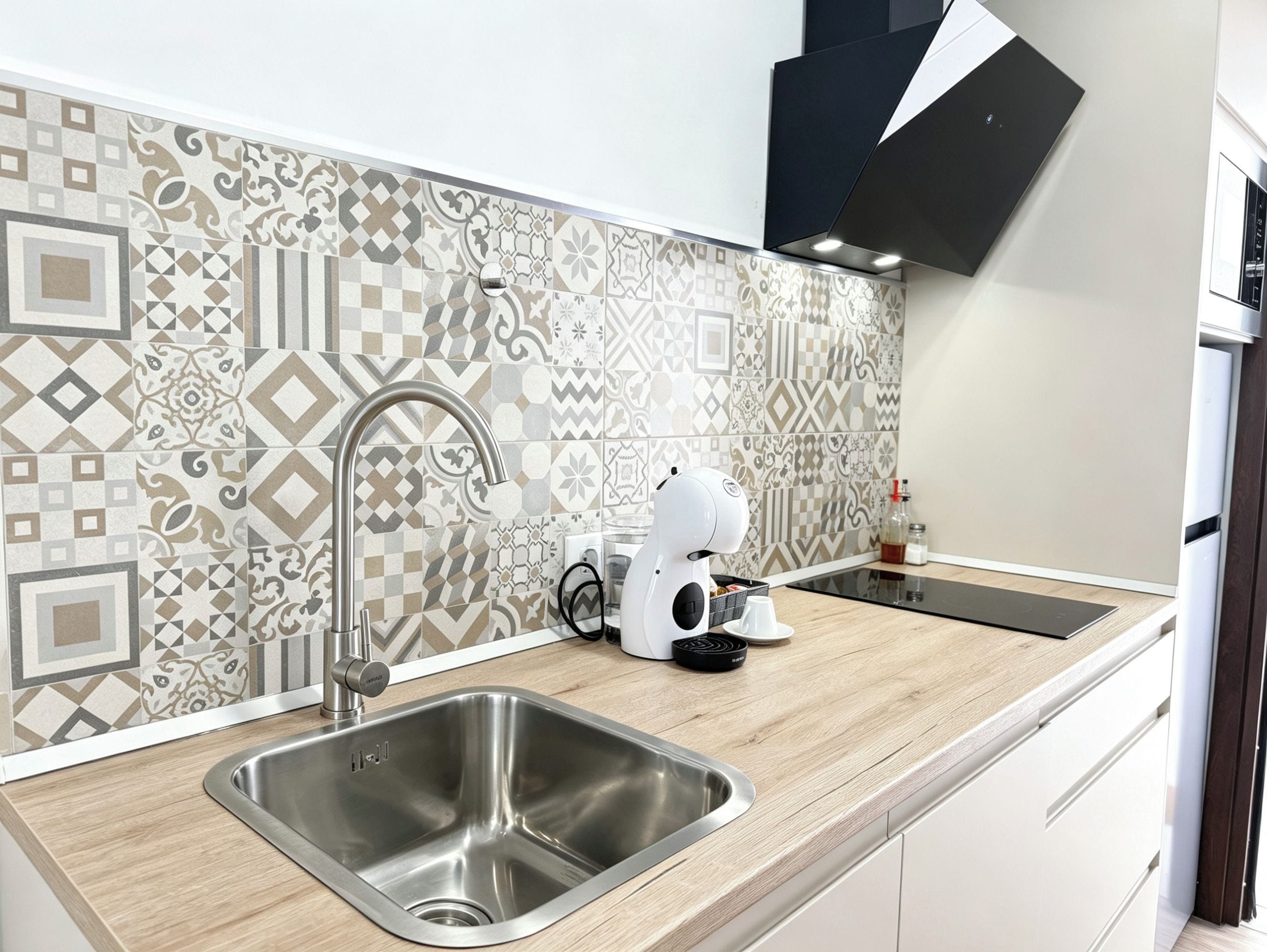 A modern kitchen with a stainless steel sink, a coffee machine, and patterned backsplash tiles.