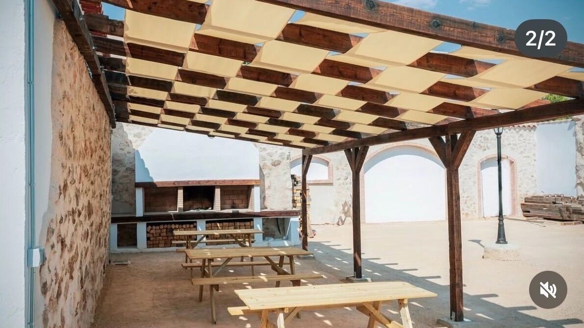Een terras buiten met houten tafels en een barbecuehoek.