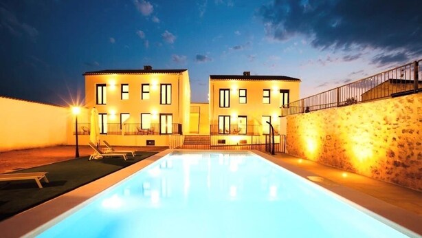 A swimming pool with two buildings in the background, one with a balcony and the other with a stone wall. - Complejo La Serrería (Belmonte)