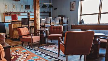 A cozy room with a wooden floor, a patterned rug, and orange chairs. There is a bar area with shelves and a sign, and a window with a view.