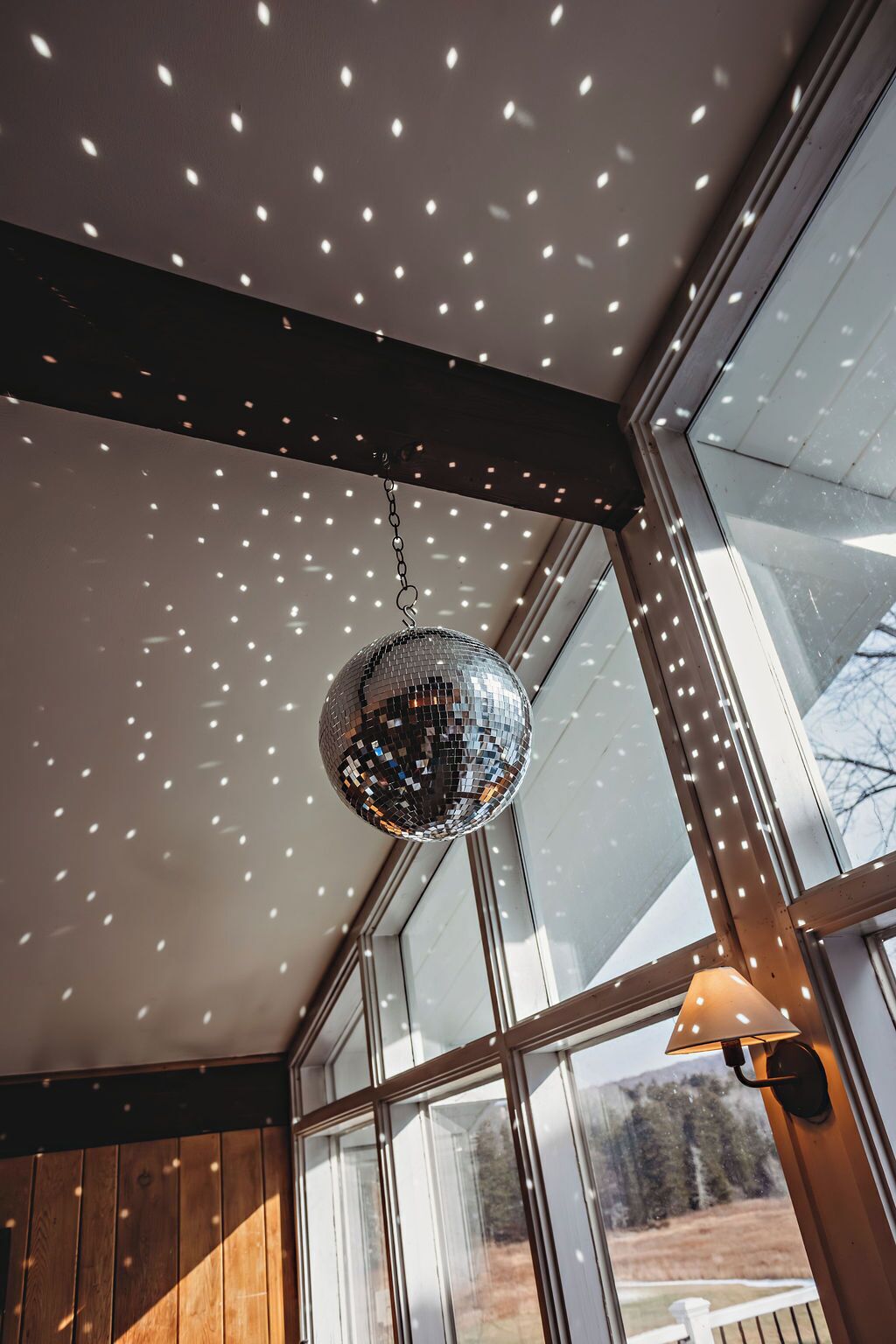 Una bola de discoteca colgando del techo en una habitación con ventanas amplias y paneles de madera.