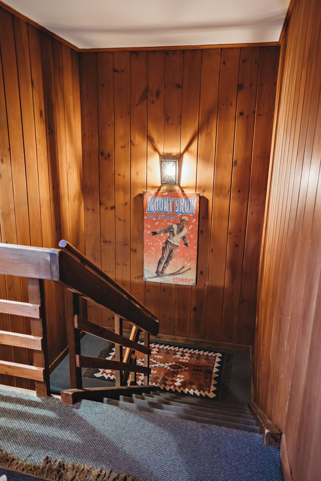 A wooden interior with a staircase, a poster advertising a mount show, and a wall-mounted light fixture.