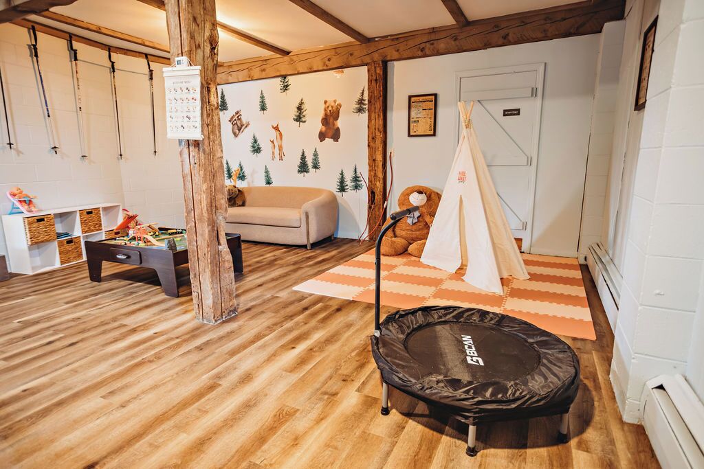 Una habitación con suelo de madera, un sofá, un trampolín, una tienda de campaña y una pared con diseños de animales.