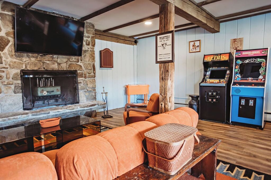 A cozy living area with a stone fireplace, orange seating, arcade games, and a mounted TV.